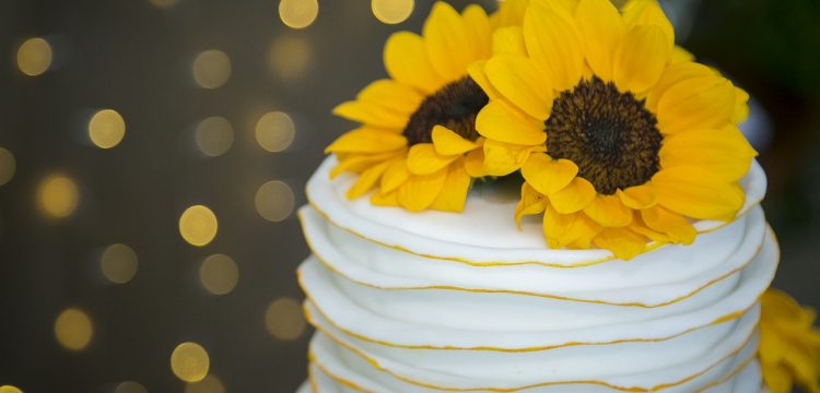 A single tiered wedding cake with a sunflower on top.