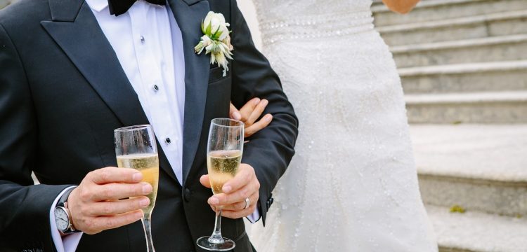 Groom holding two flutes of champagne.