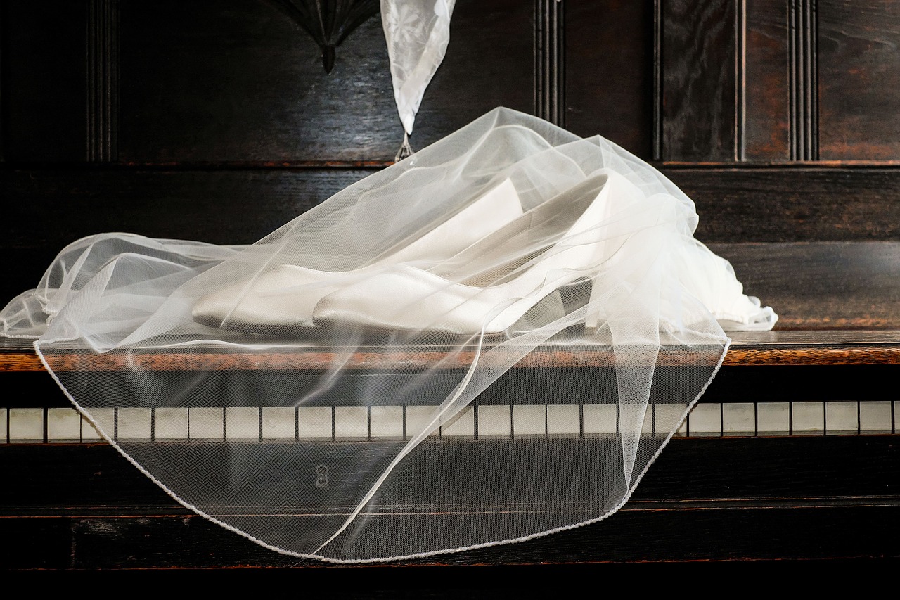 Wedding veil and shoes laying on a piano.