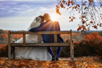 Bride and groom sitting on a bench in Fall.
