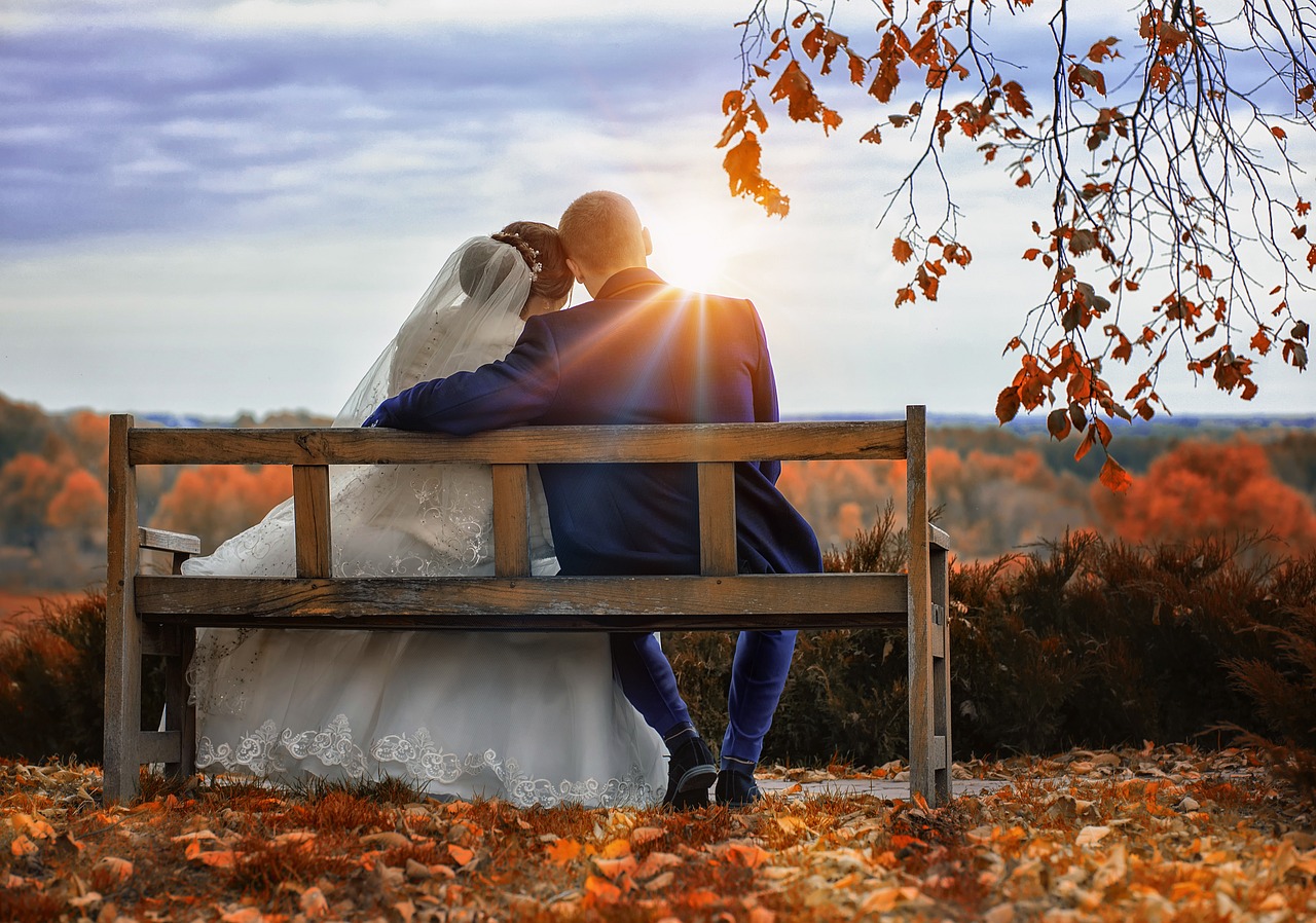 Bride and groom sitting on a bench in the Fall.